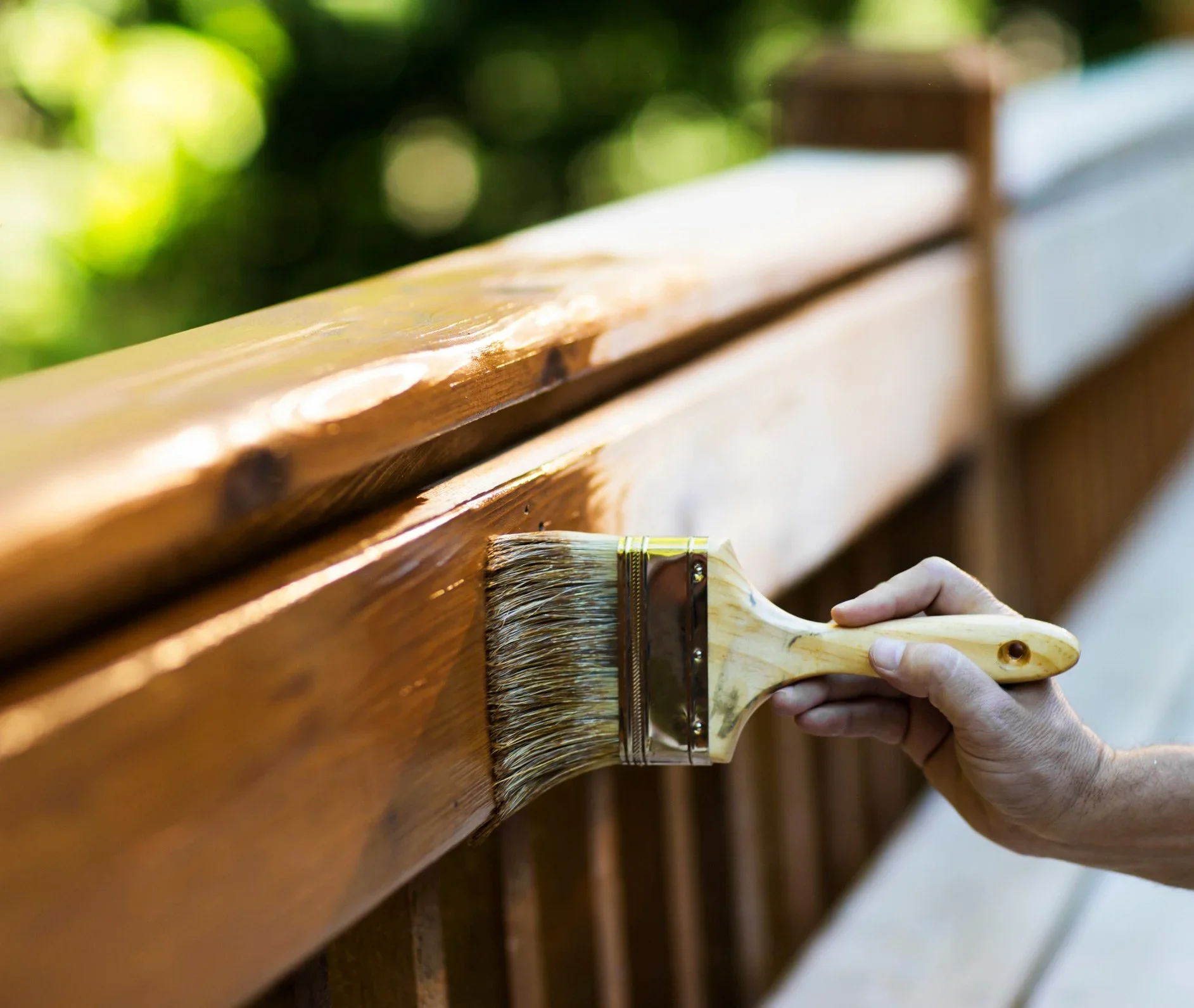 Person applying Treatex natural wood finish oil to outdoor timber balcony railing with brush