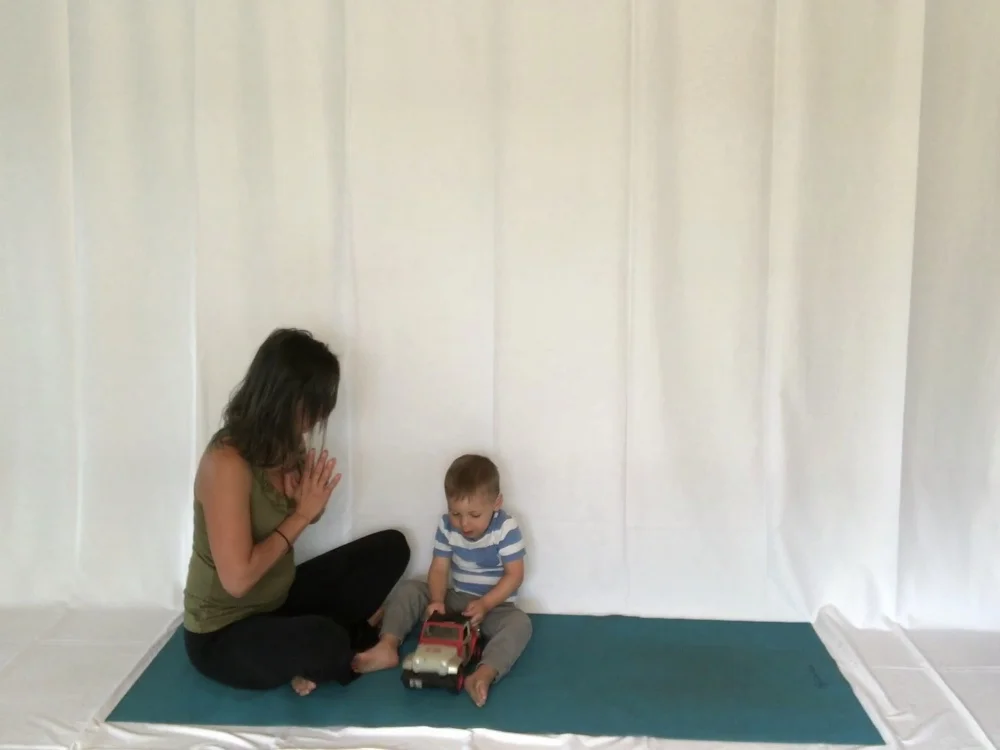 Mama, Seated with her hands clasped together in a prayer pose at her heart.