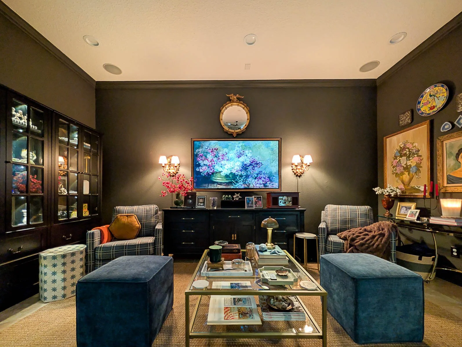 A moody, curated living room featuring a brass coffee table styled with linen-bound book stacks, a marble tray, and organic textures against a dark gallery wall.