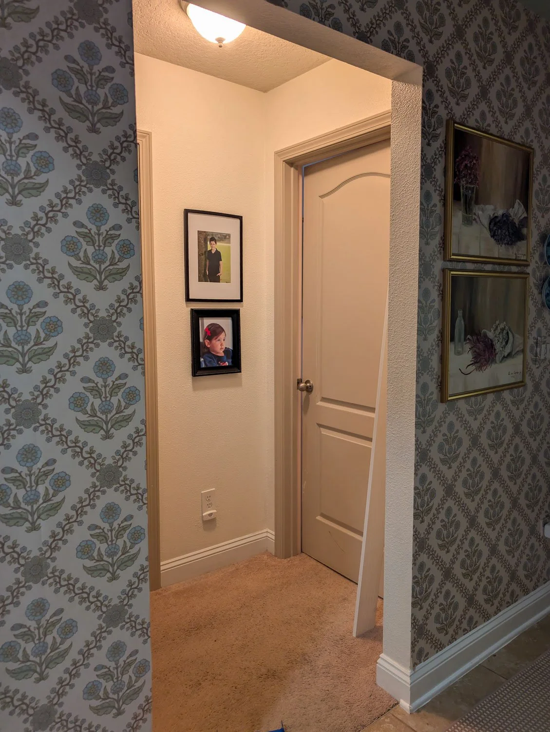 A long piece of white molding leans against a wallpapered wall near a hallway as part of a home renovation project.