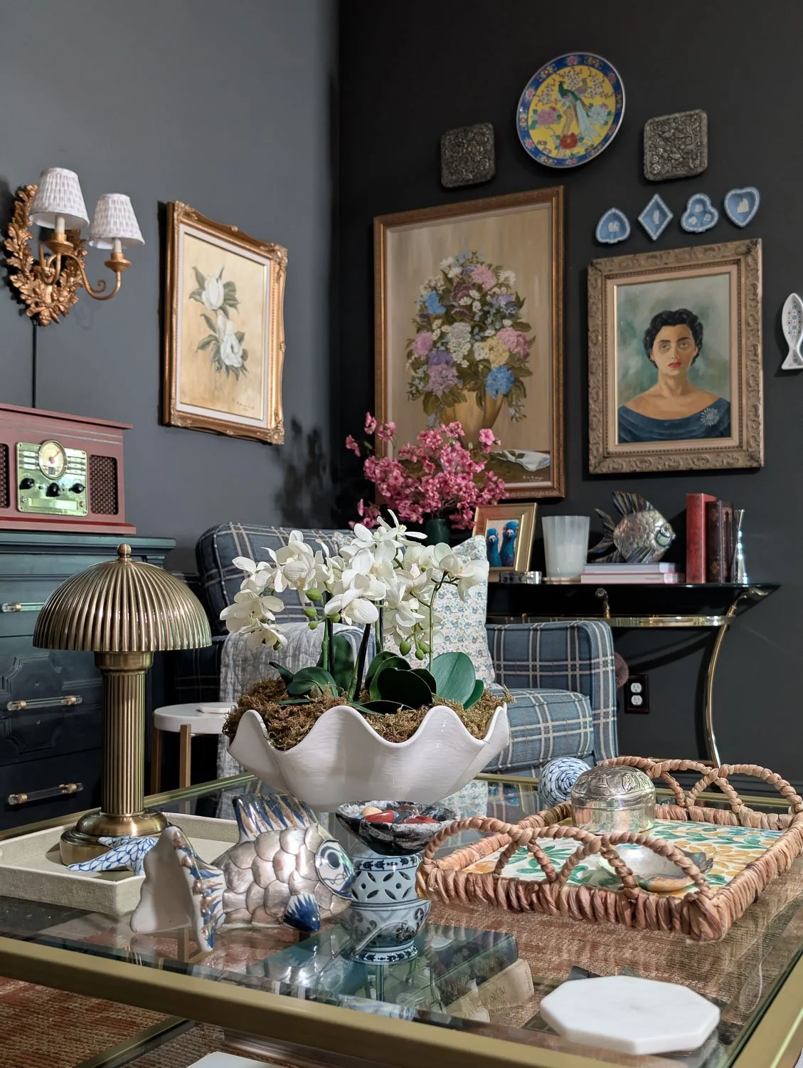 A warm wood media console styled for summer with a basket vase of vibrant yellow branches, leaning framed art, and a vintage-style radio against deep charcoal gray walls in a modern heritage living room.
