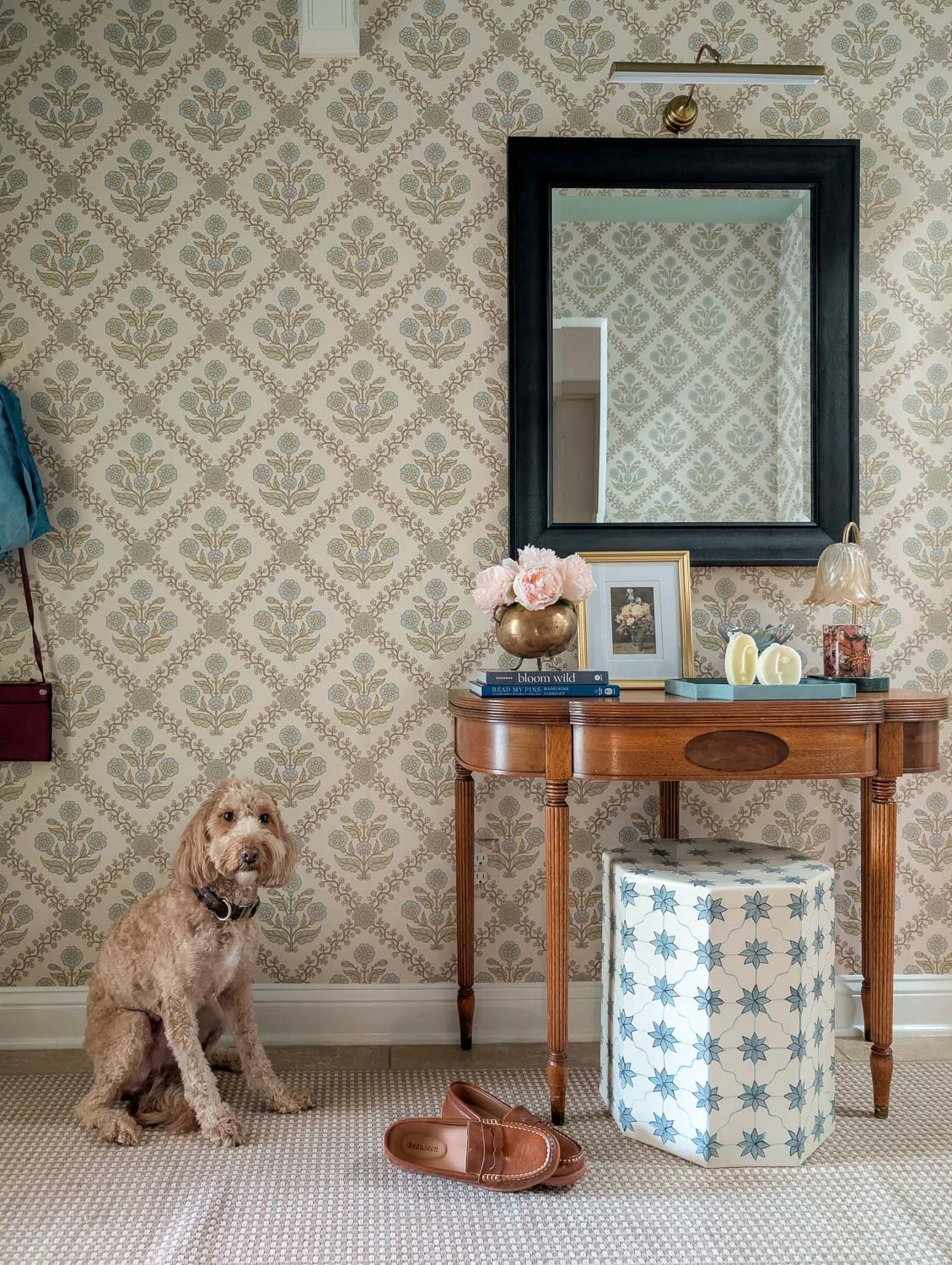 A goldendoodle sits on a neutral rug in a Grandmillennial entryway featuring blue floral damask wallpaper and a vintage wooden console table.