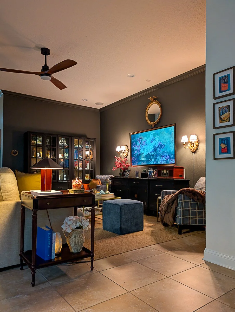 An inviting living space showcasing layered lighting from a ceiling fan, recessed lights, and a table lamp, with dark walls and a large black sideboard.