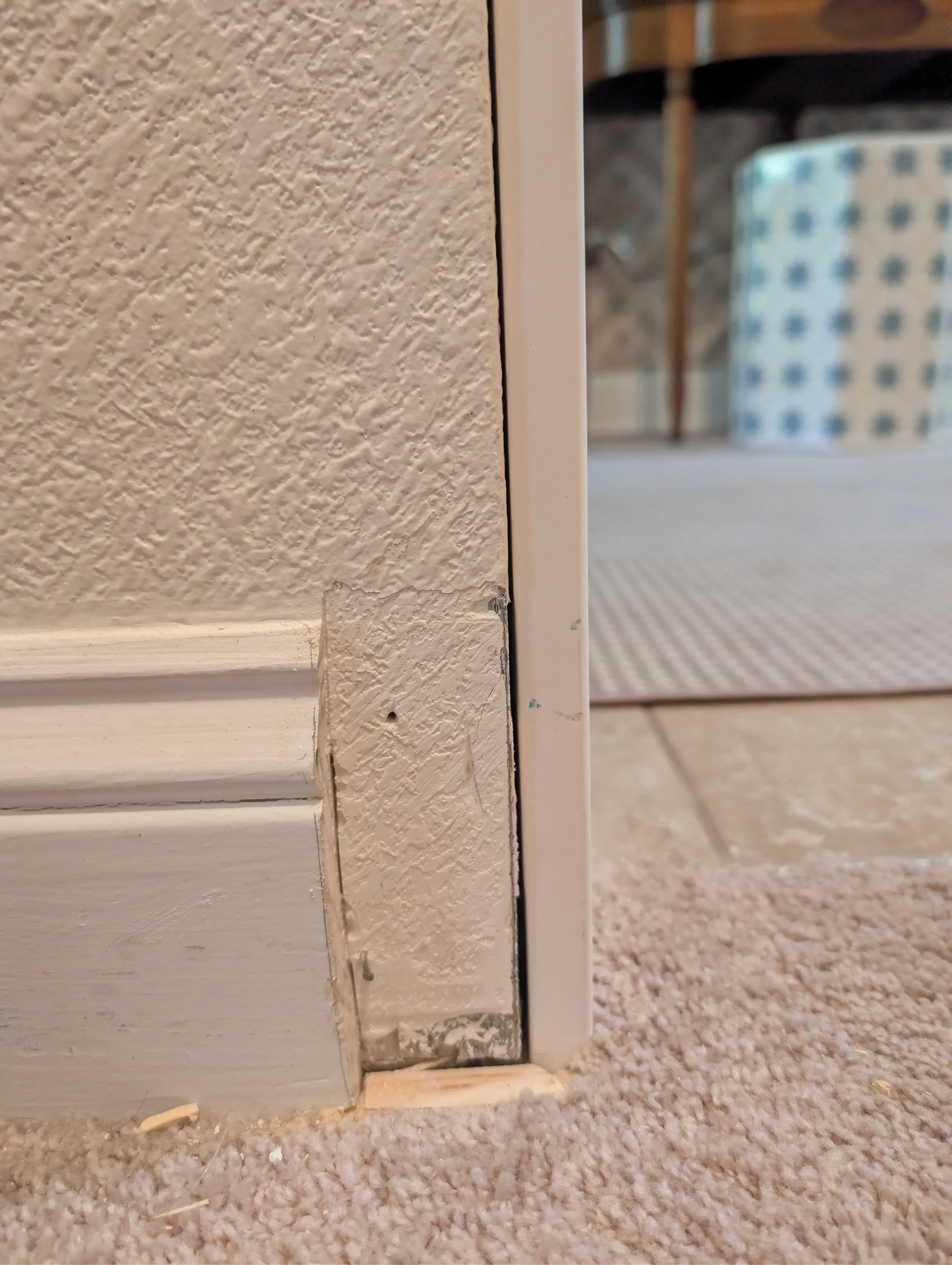 A close-up view shows a section of white baseboard that has been cut away to reveal the textured drywall and a metal corner bead underneath.
