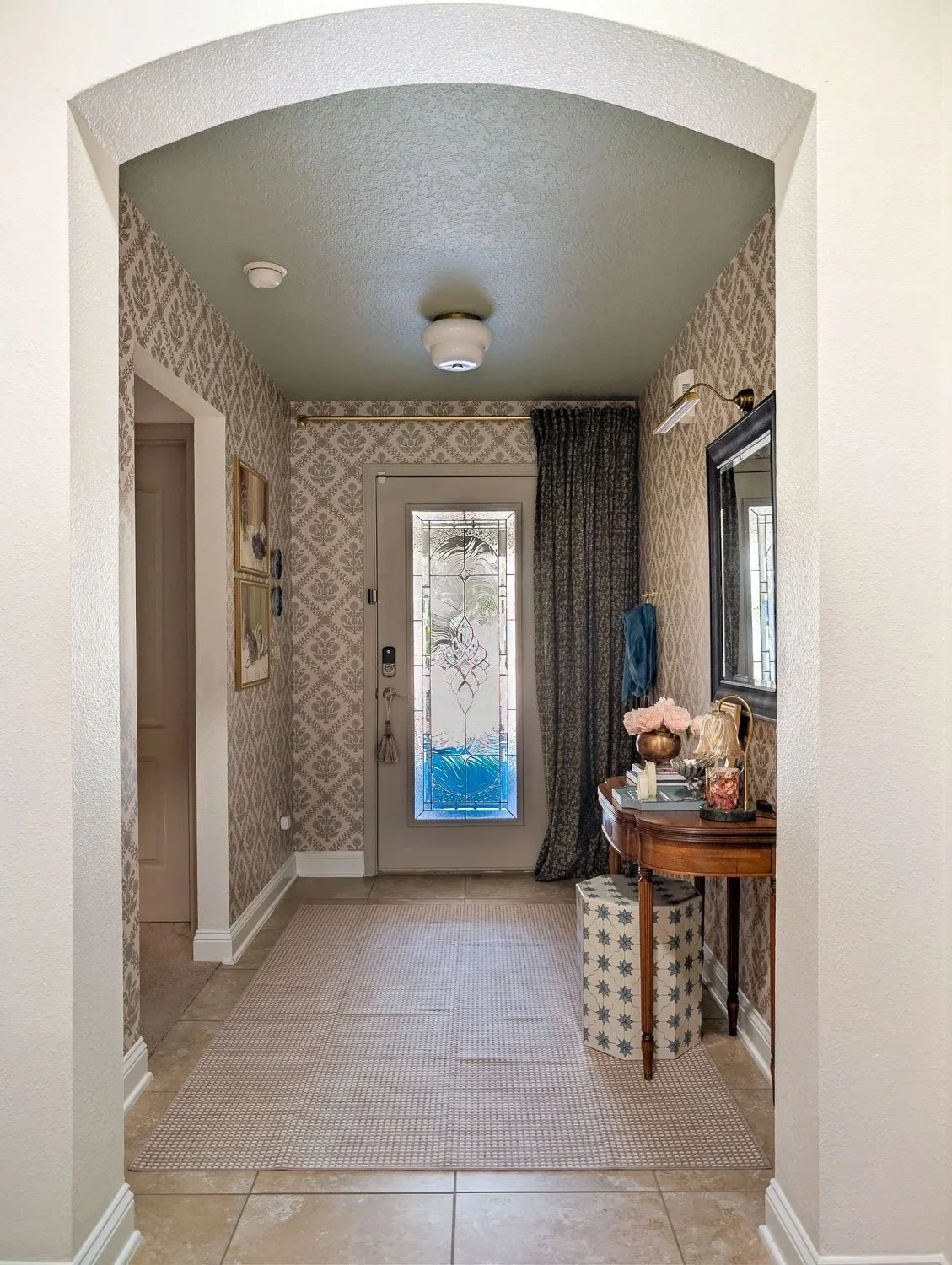 A wide view of a Moody Traditional entryway makeover featuring patterned floral wallpaper, a sage green ceiling, and a neutral runner rug leading into an arched hallway.