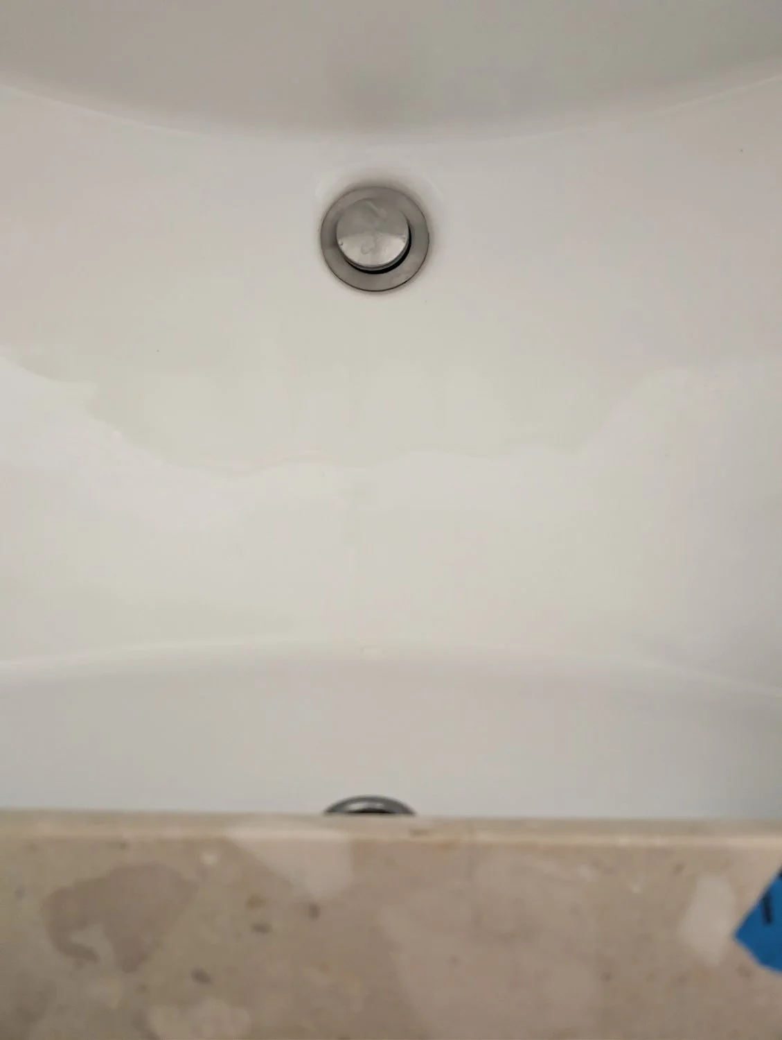 An overhead view of a completely clean, repaired white porcelain bathroom sink with a smooth basin, showing a seamless finish near the sink drain and marble countertop.