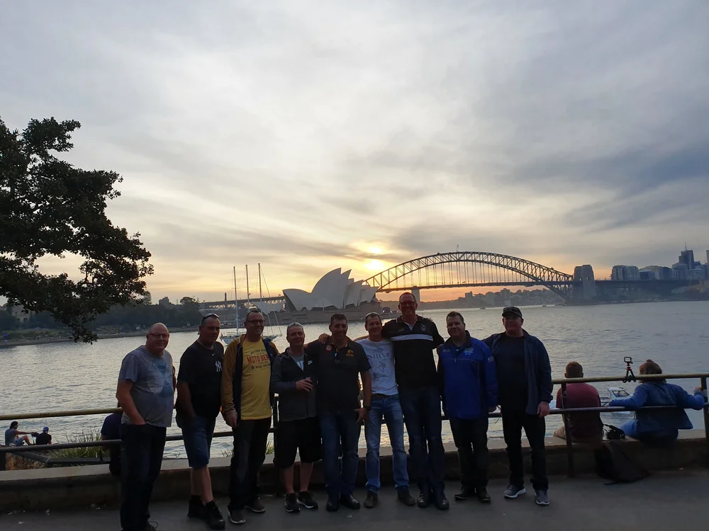 A private tour group at Mrs Macquarie's Point at sunset, with the Sydney Opera House and Harbour Bridge behind them