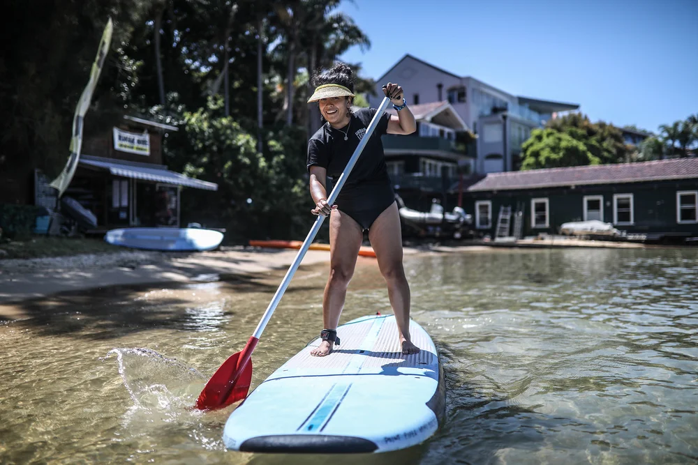 A guest stand-up paddle boarding off the beach at Rose Bay during a private Sydney tour