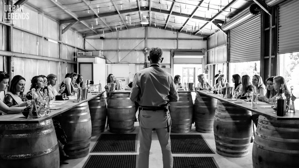 A host leading a seated tasting at barrel tables inside a Hunter Valley winery