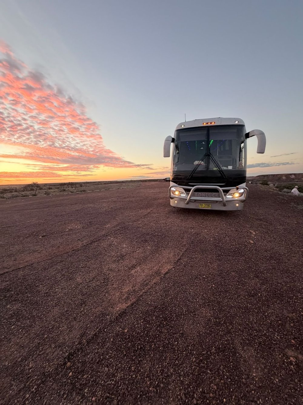 Urban Legends luxury coach on red dirt under an outback sunrise, on a coach tour to Uluru