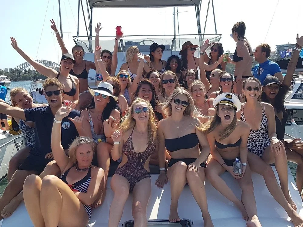 Birthday group celebrating with their arms up on the foredeck of a Sydney Harbour party boat