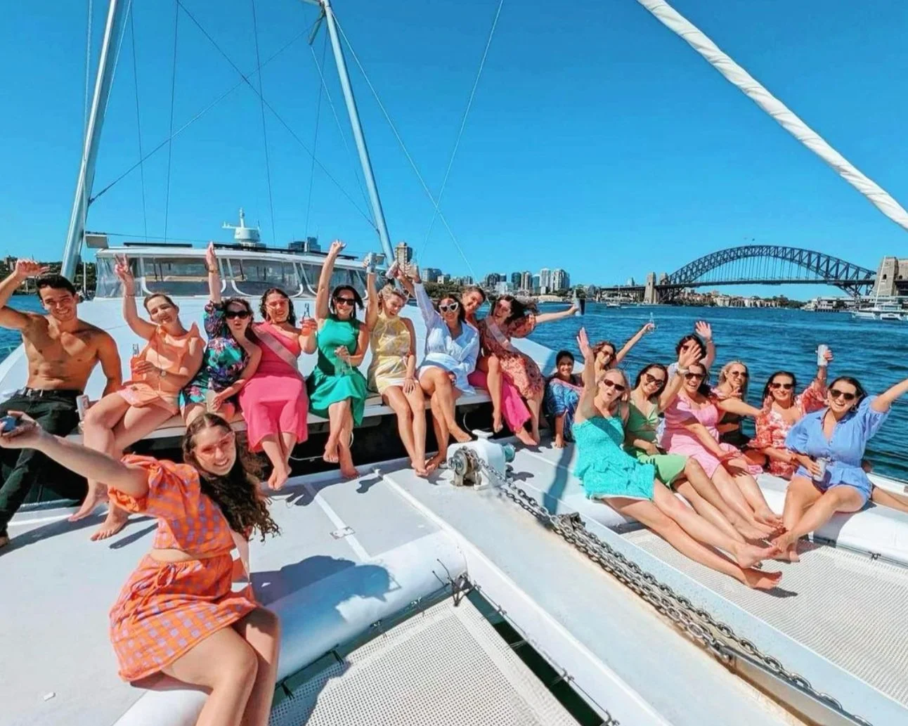 Guests relaxing on the foredeck nets of a Sydney Harbour catamaran charter with the Harbour Bridge behind