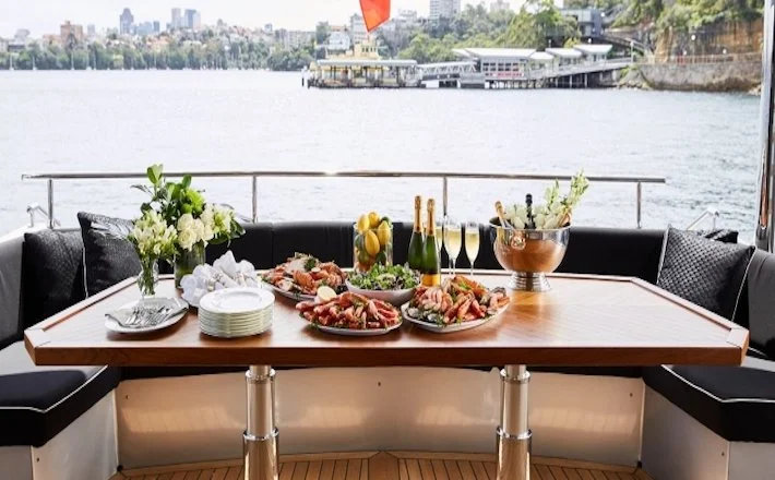 Banquet table set with grazing platters, champagne on ice and fresh flowers on the aft deck of a charter yacht on Sydney Harbour