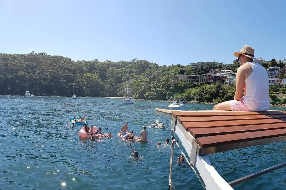 Charter guests swimming off the swim platform of a yacht anchored in a sheltered Sydney Harbour bay