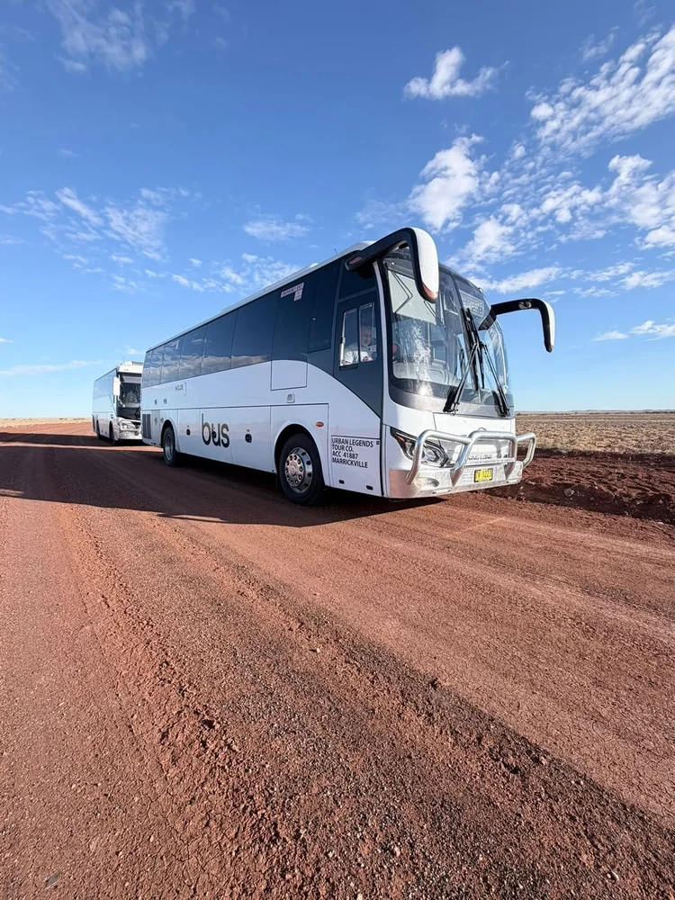 Urban Legends coach charter parked on red dirt under a big blue outback sky
