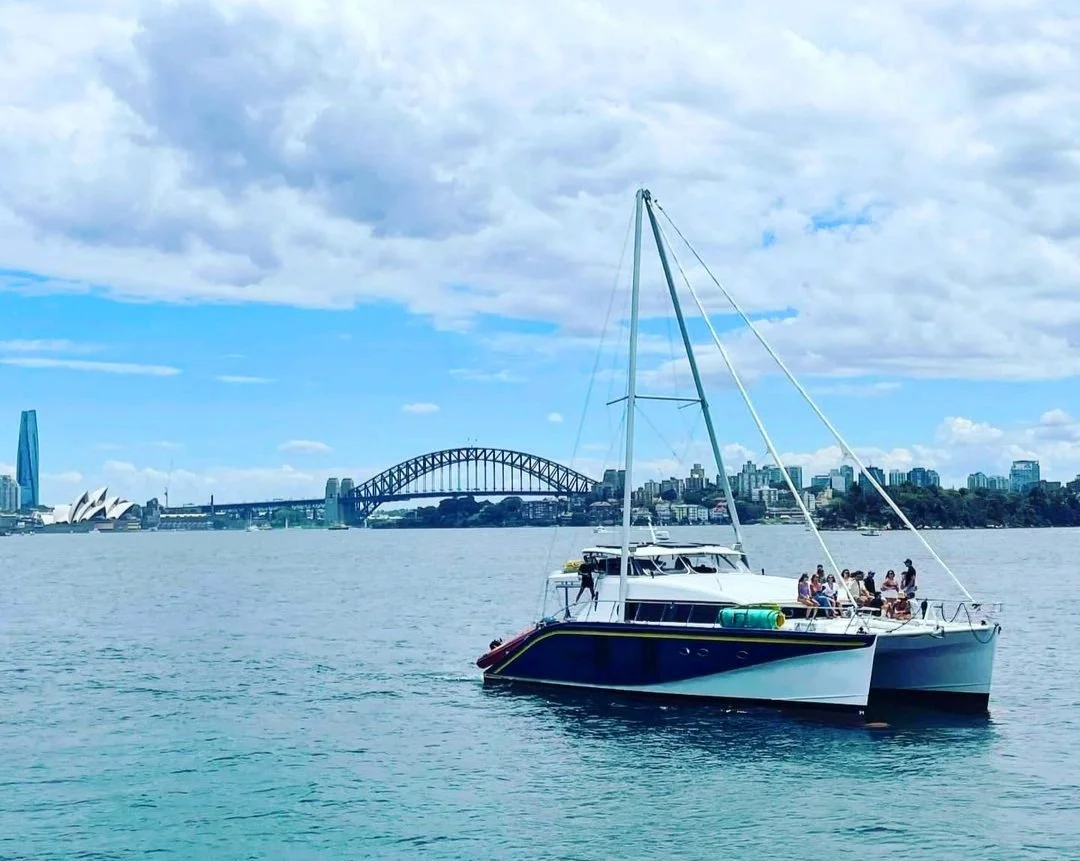 Charter catamaran with guests on deck crossing Sydney Harbour with the Harbour Bridge in the background