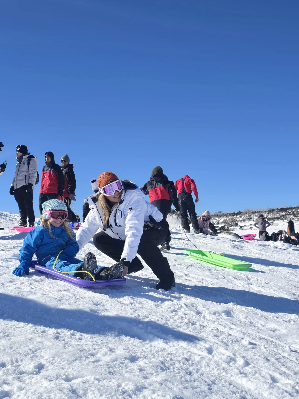 Mum pushing her daughter on a toboggan under blue skies on a snow tour from Sydney