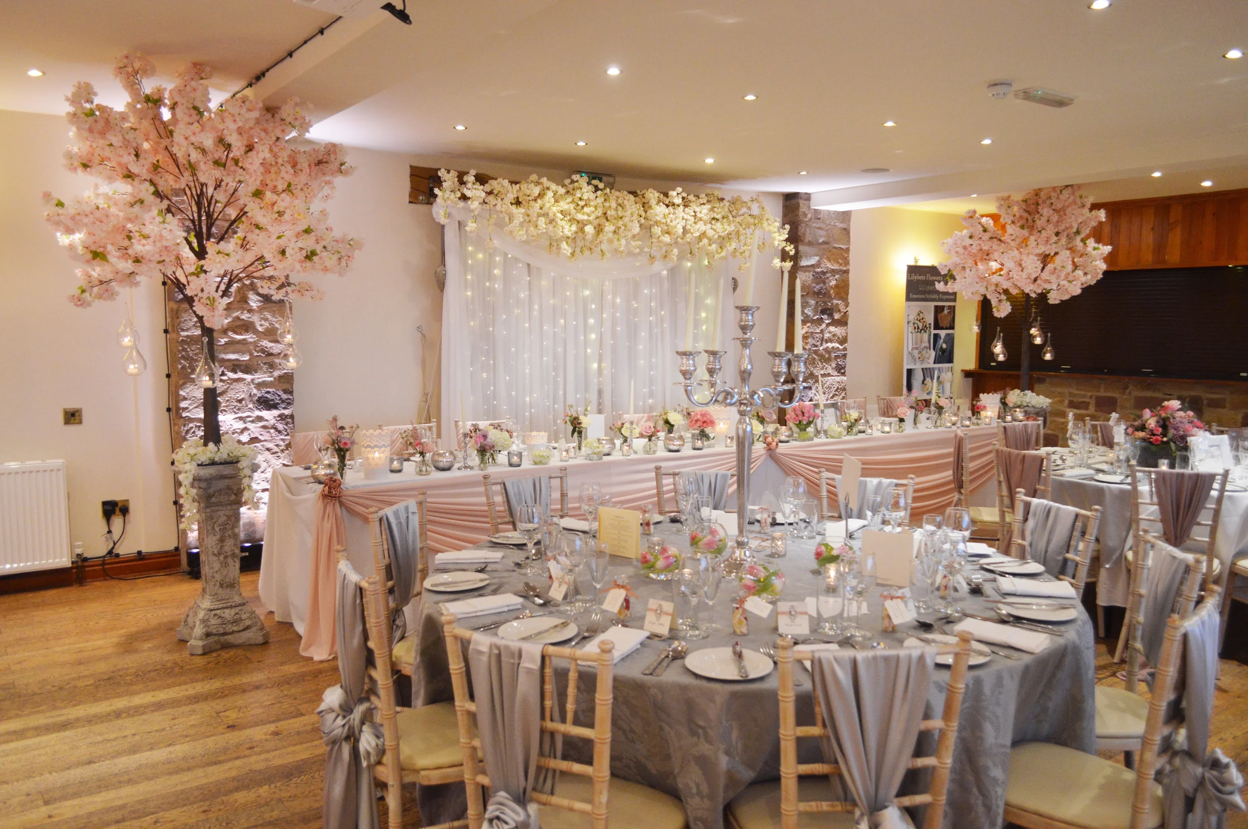 Pink blossom trees on pillars, hanging flowers on fairy light curtain and top table drape