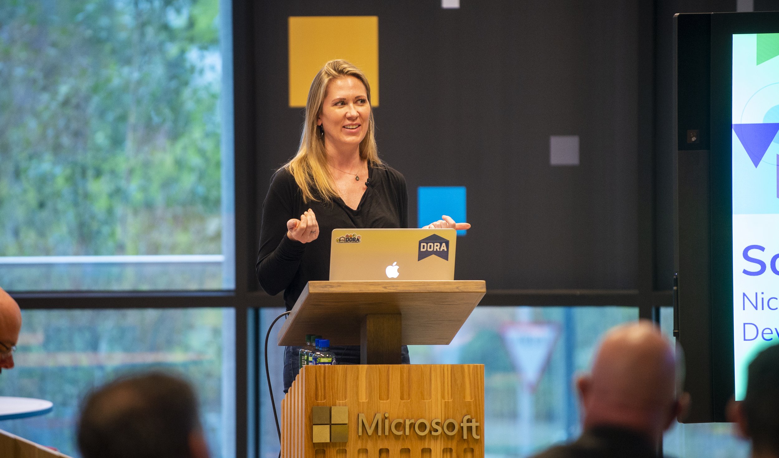 Dr. Nicole Forsgren, the brains behind DORA (DevOps Research and Assessment), giving a presentation on a podium with her computer.