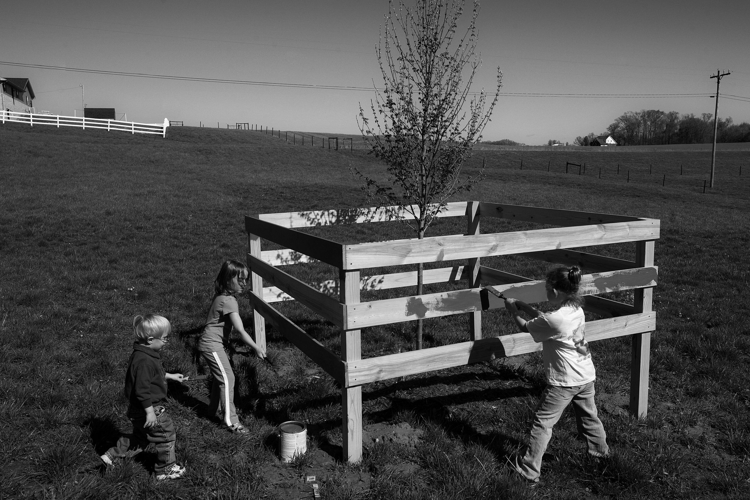 As a memorial to Red, who died of complications of Parkinson’s disease, his family gathered to paint a fence around a young red sunset maple tree that was planted in the pasture on the family property. Kash Kendall, 2, left, and his cousins Merin Bu
