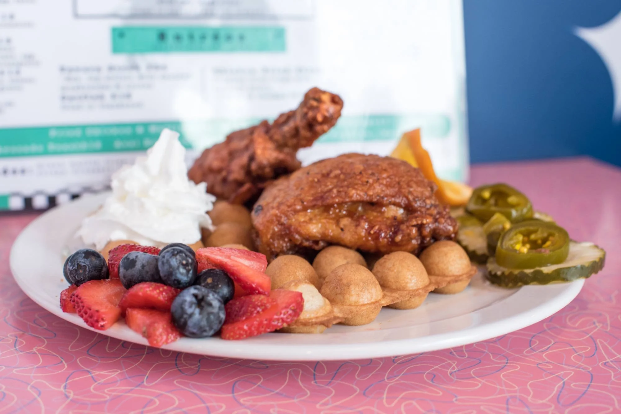 Plate of fried chicken, waffle, whipped cream, strawberries, blueberries, jalapenos, and sides.