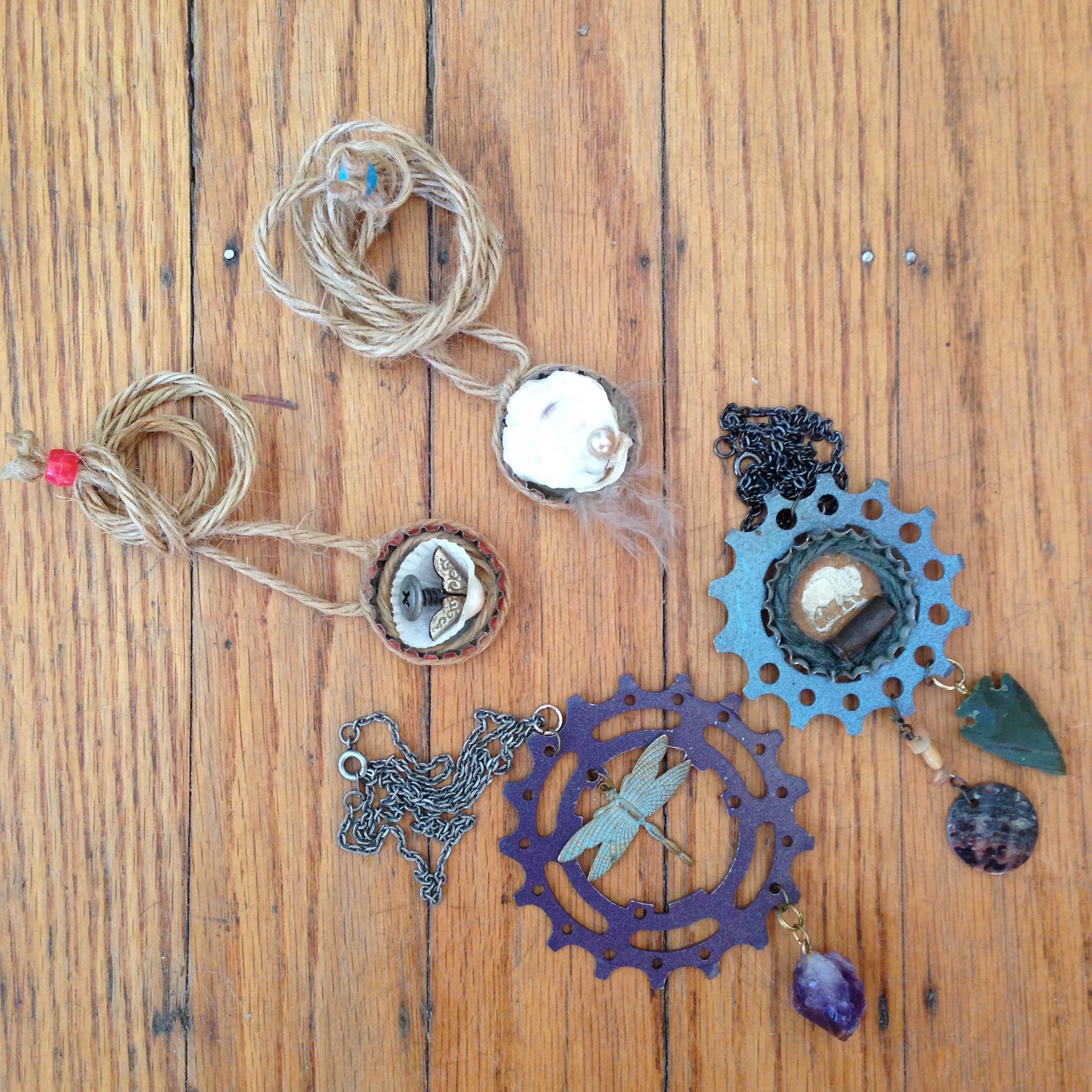 Adjustable bottle cap necklaces and bicycle gears on chains with gemstones.