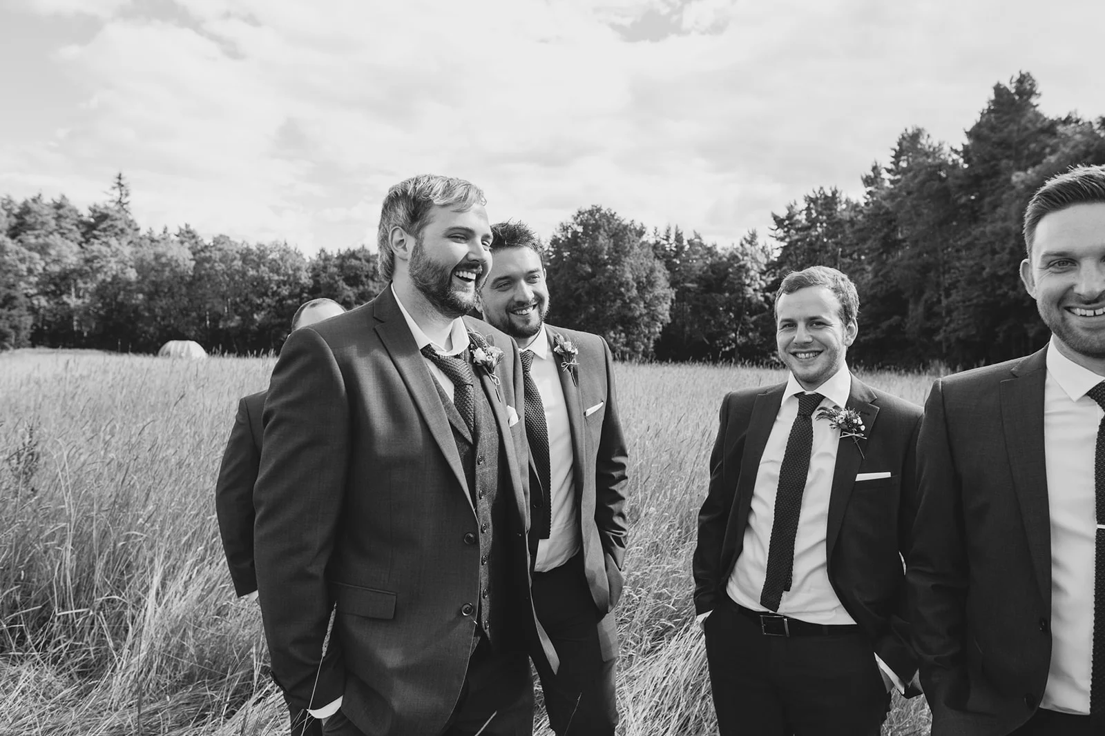 a groom and the groomsmen stand laughing together in a field. camp katur wedding north yorkshire tipi wedding venue glamping. stop motion wedding films uk