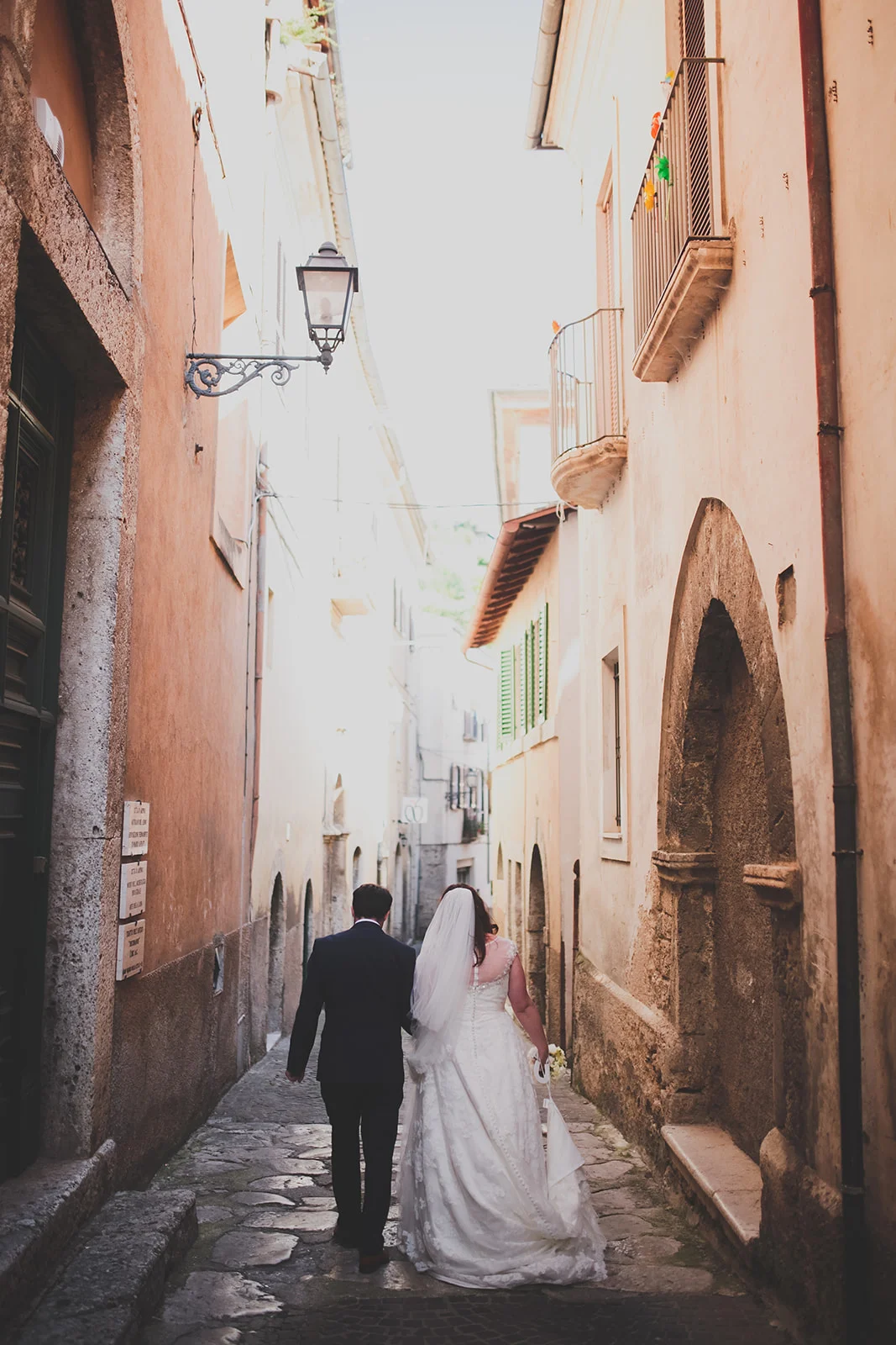 a bride and groom walk down a tall italian street. destination creative wedding photography italy. stop motion wedding films uk