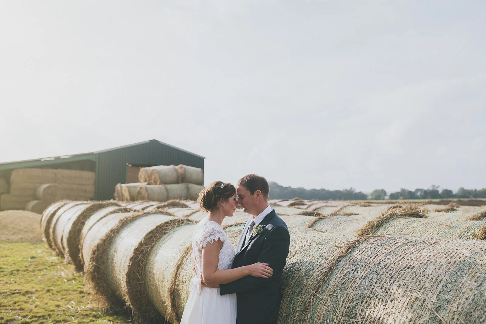 bride and groom are close, standing in front of a barn and haybales. star inn at harome near helmsley, north yorkshire wedding photographer. stop motion wedding films uk.