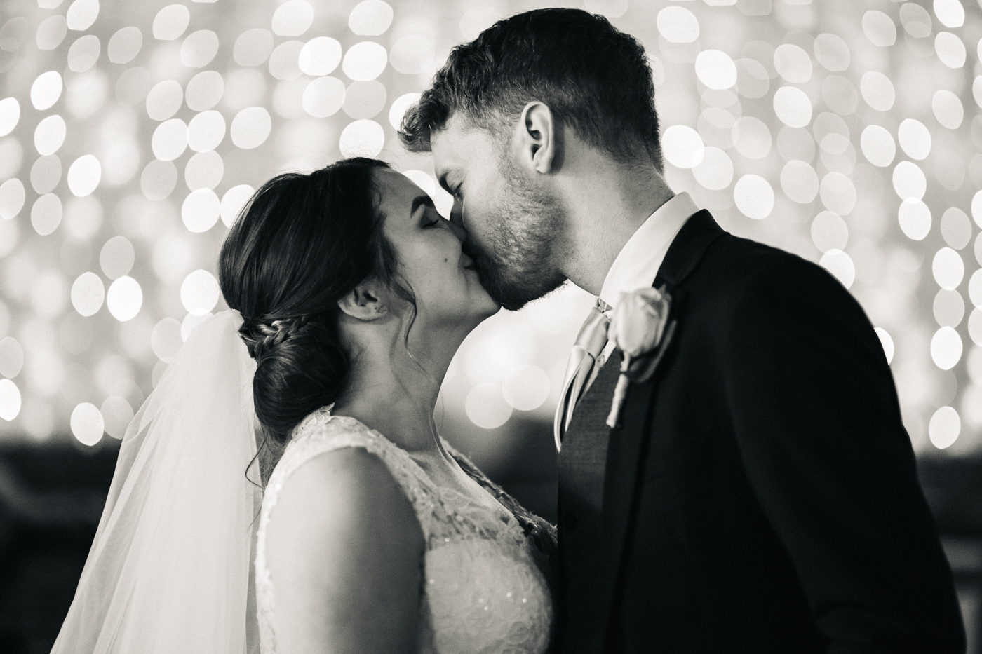 the bride and groom kiss in front of fairylights. spring barn wedding at east riddlesden hall keighley west yorkshire wedding photographer
