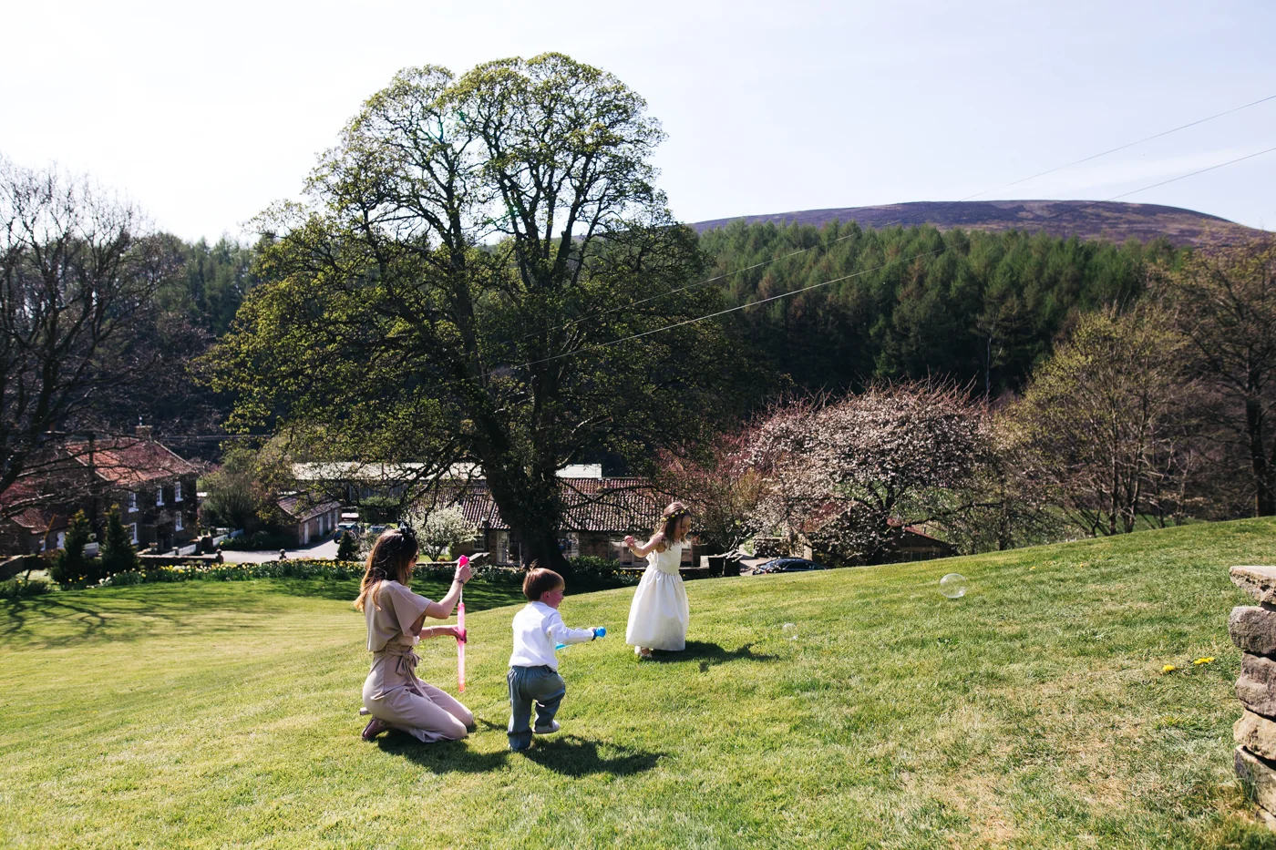 two children and a women play with a bubble wand on the grass. wedding at laskill house north yorkshire helmsley wedding photographer north east teesside
