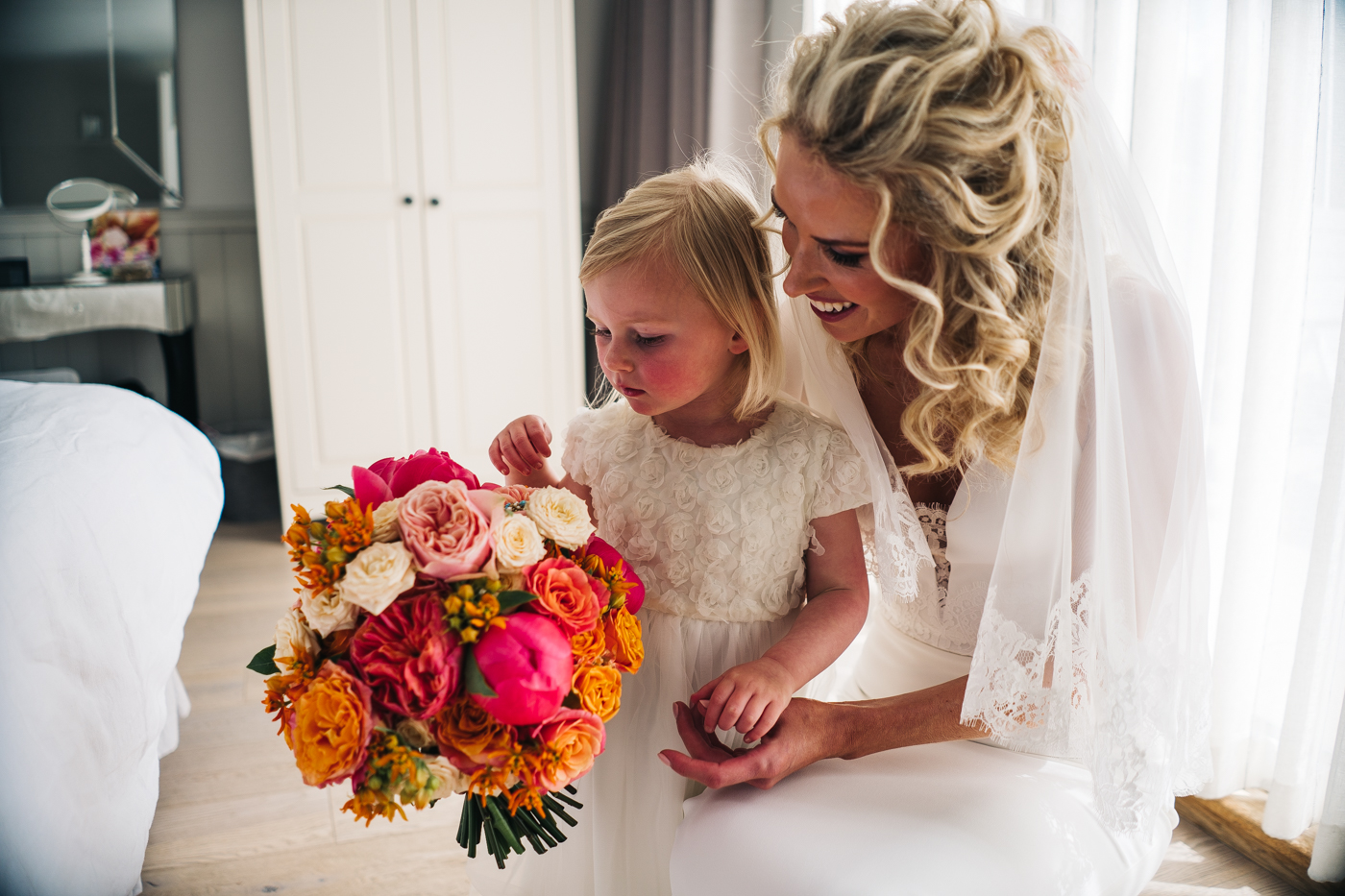 a bride and her flower girl cuddle and look at her bouquet. photo by sally t photography, wedding at ever after, tavistock, devon photographer