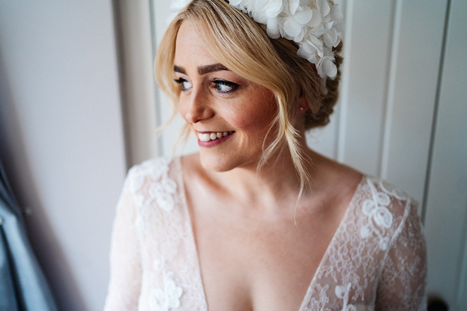 bride in a lace marrime dress and oversized headband smiles looking off camera to the left