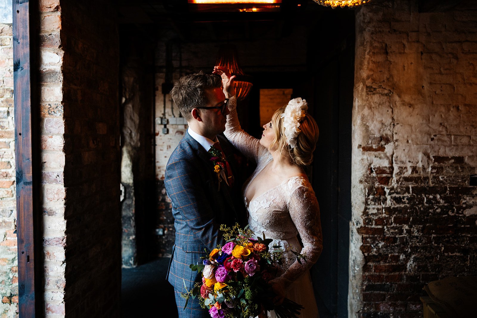 bride gently touching groom's head, in a barn, colourful flowers the normans York wedding