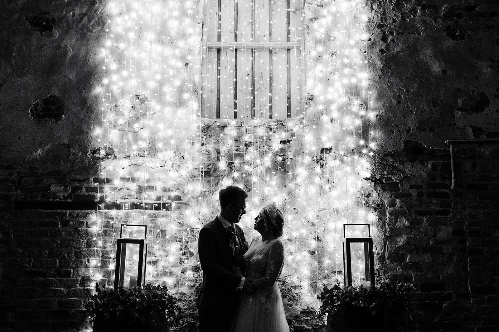 black and white back-lit image of a bride and groom in a fairy light-lit barn room. the normans York wedding