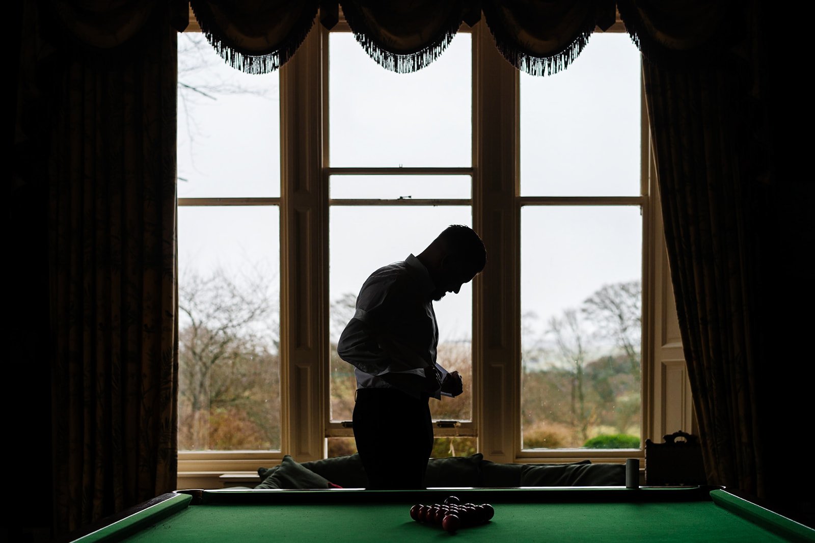 blacklit shot of a groom getting dressed in a snooker room at toftcombs mansion house in the scottish borders.