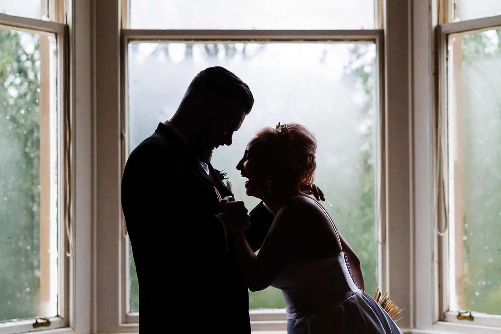 silhouette of a bride and groom laughing towards each other with a window behind them. wedding at toftcombs in Scotland