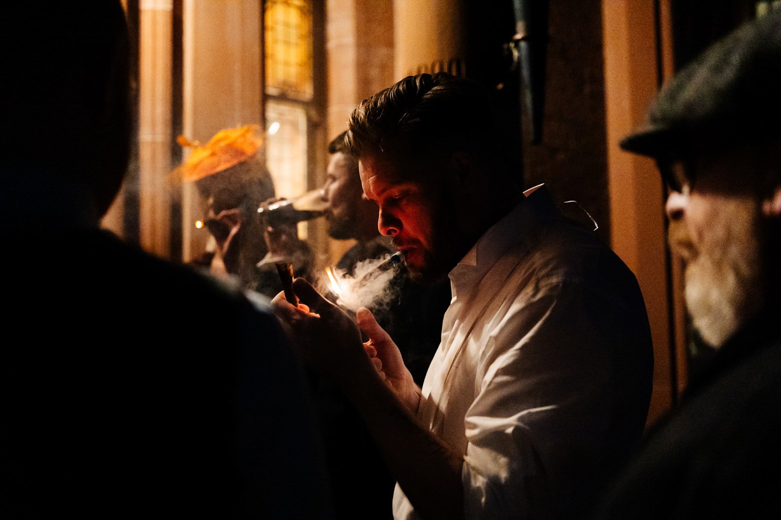 groom lights a cigar outside toftcombs mansion house. golden light and smoke surrounds him