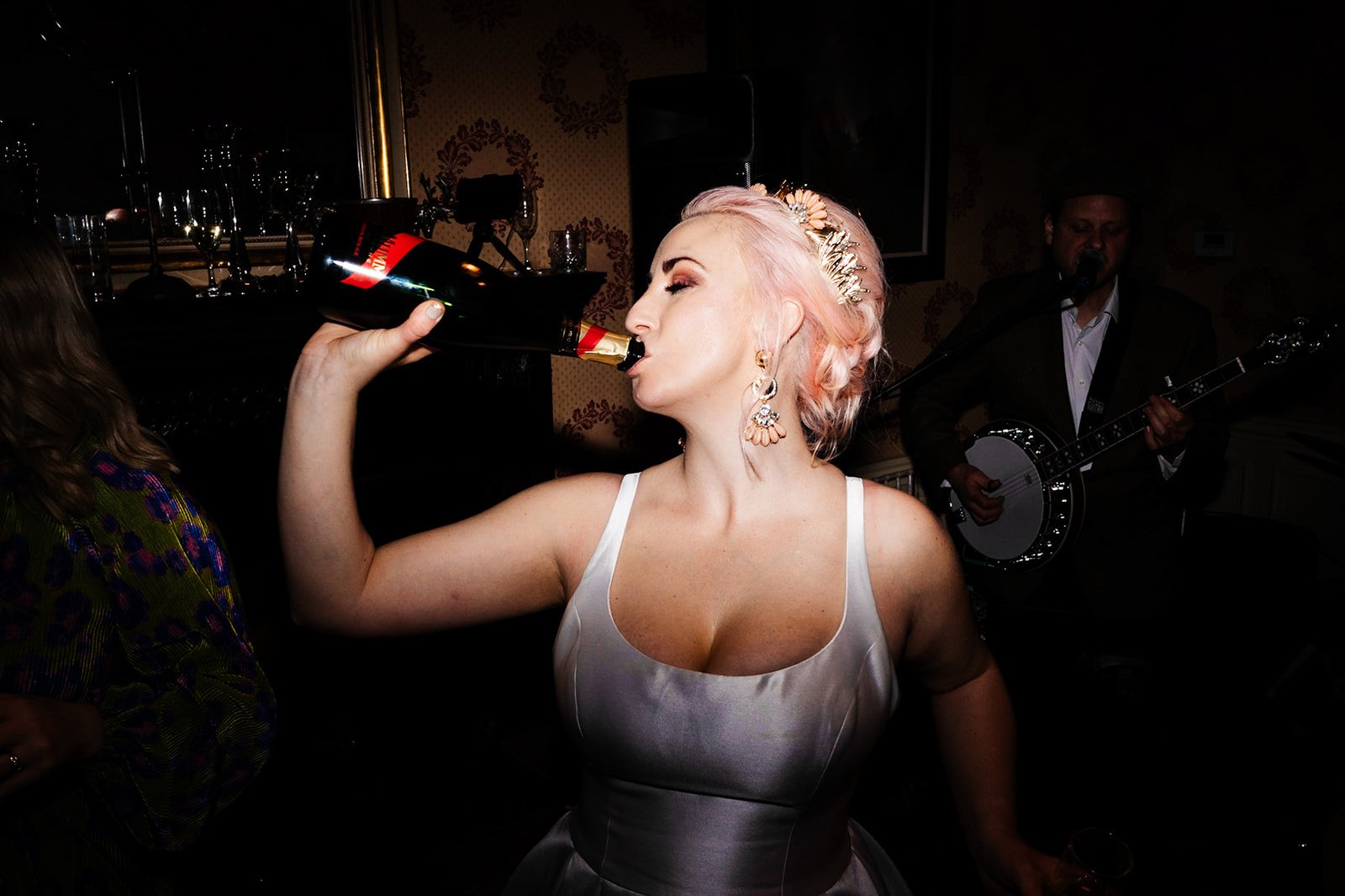 bride with pink hair necks champagne on the dance floor. a smokey atmospheric shot of the bride and groom cheering and dancing. wedding at toftcombs in Scotland