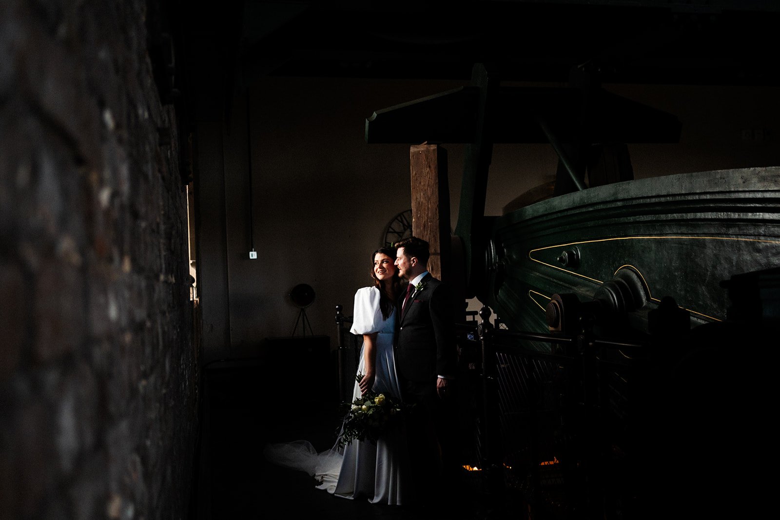 a wide shot, a dark room with the bride and groom highlighted by the side light coming in from a window. wedding at dalton old pump house 