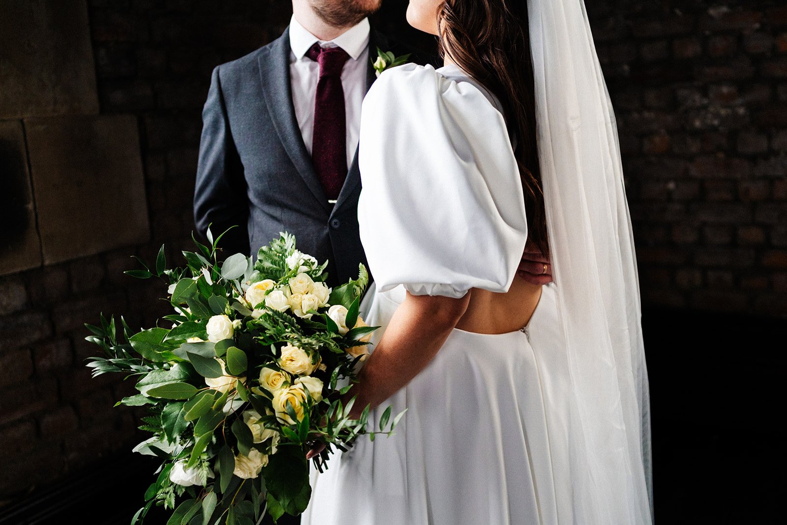 a close shot of the bride and groom standing close to each other, the detail shows her dress sleeves, his suit and her flowers. wedding at dalton old pump house 