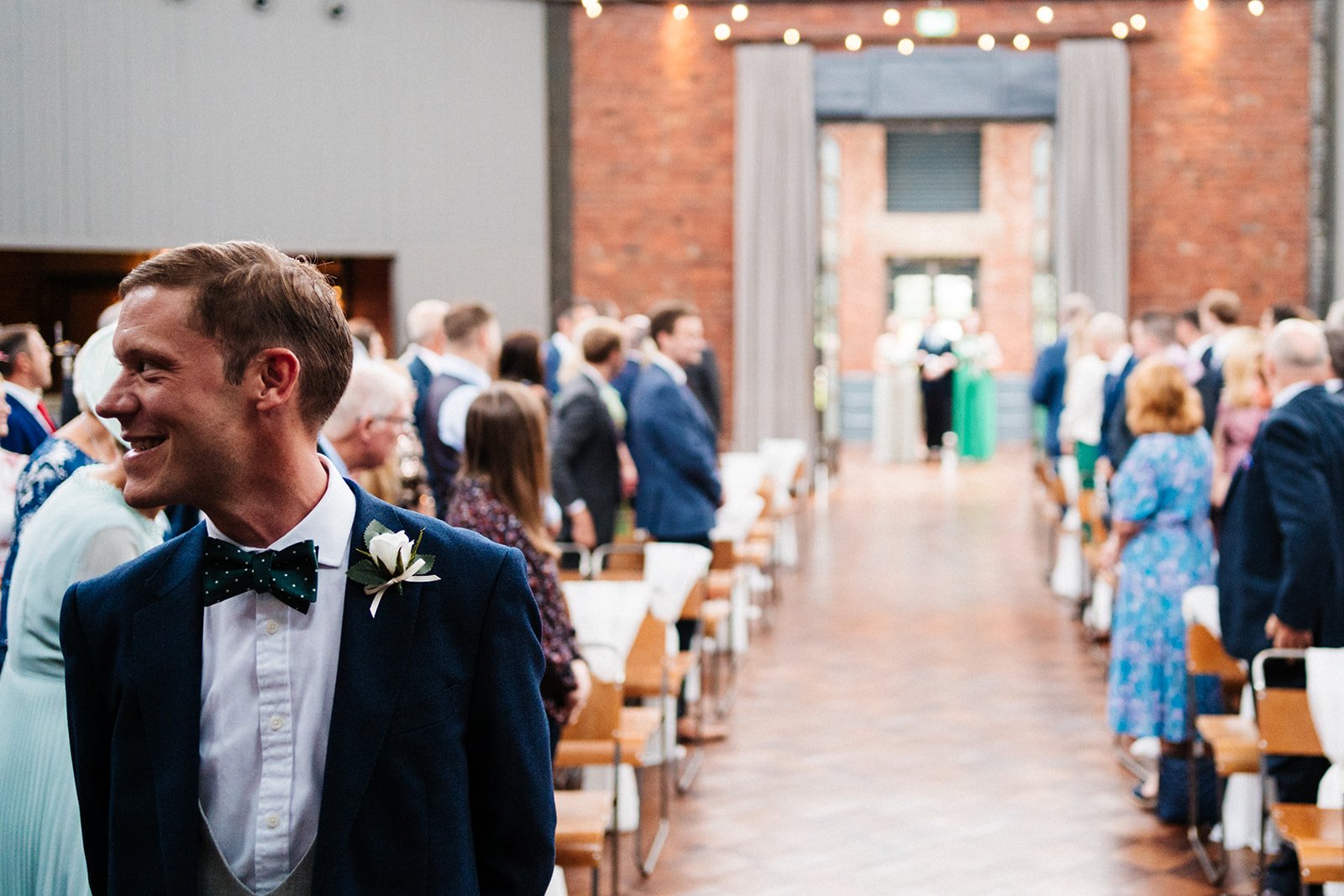 A groom looks to the side as the doors open behind him at the beginning of the wedding ceremony at Wylam Brewery in Newcastle