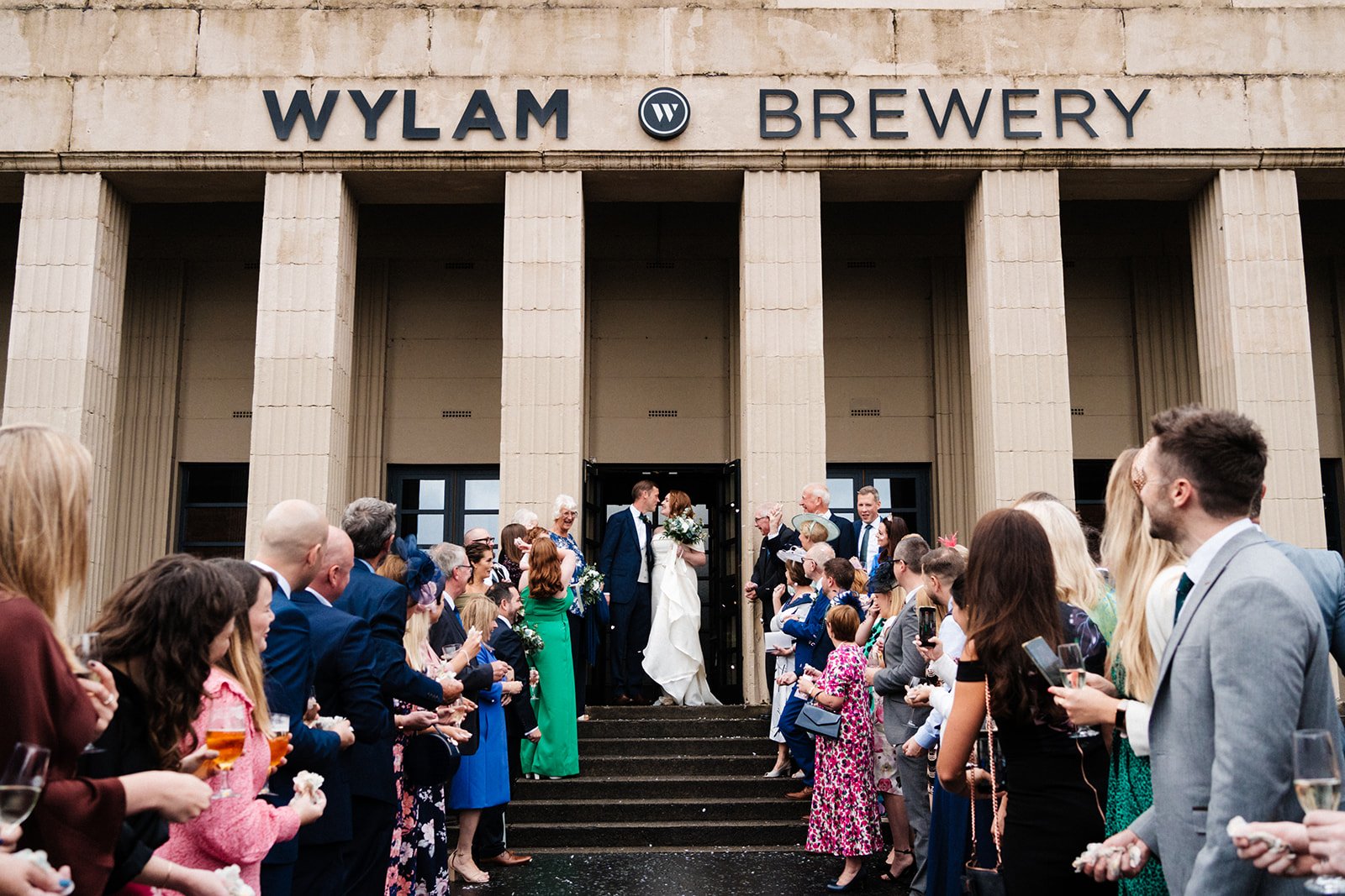 Bride and groom stand at the top of the steps about to walk through confetti outside Wylam Brewery in Newcastle. North-east wedding photography