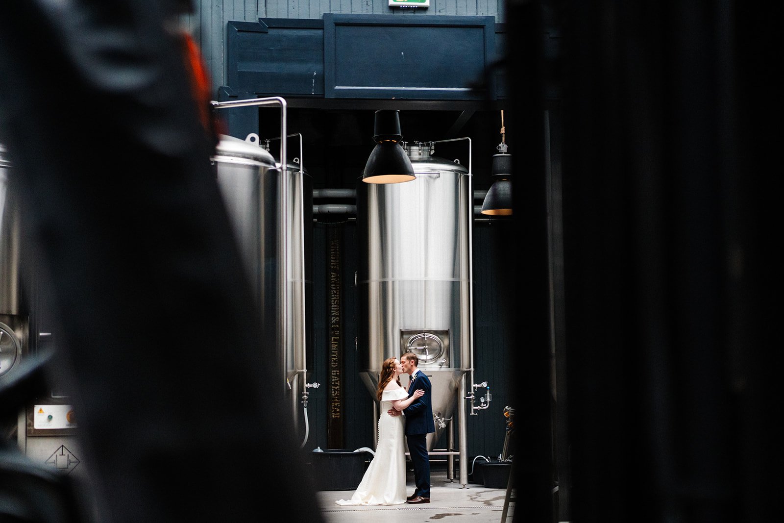 A wide shot of a bride and groom in the Brewery at Wylam Brewery in Newcastle. They are standing next to each other and smiling