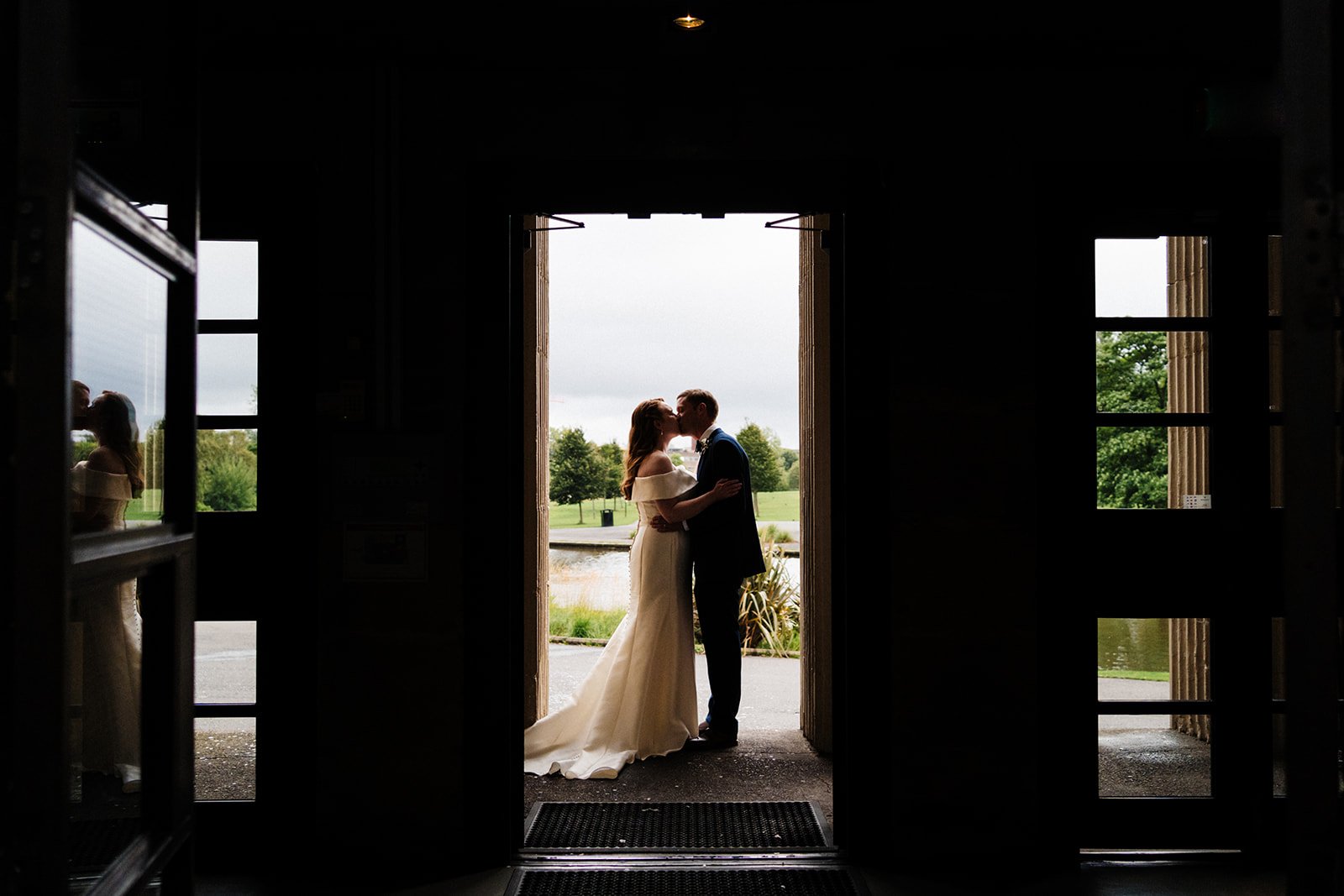 Silhouetted shot of the bride and groom shot at Wylam Brewery in Newcastle with a lake and field behind them they are kissing