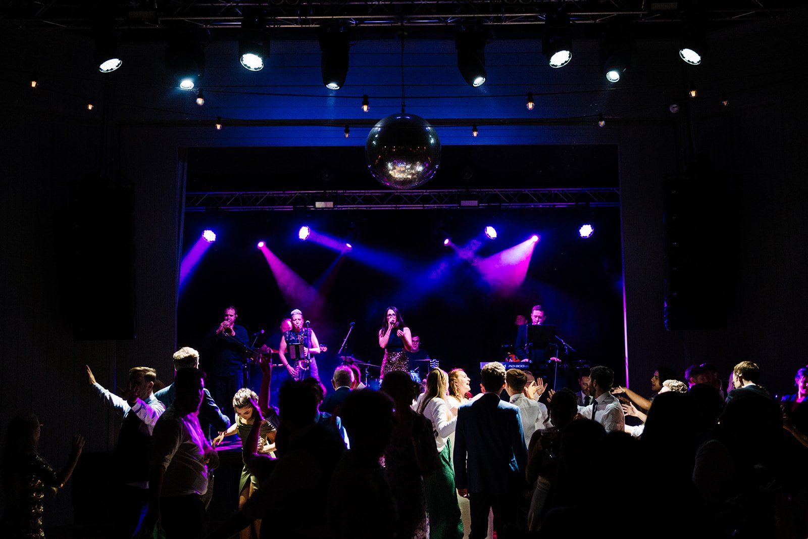 A wide shot of a purple lit band playing and guests dancing at Wylam Brewery in Newcastle