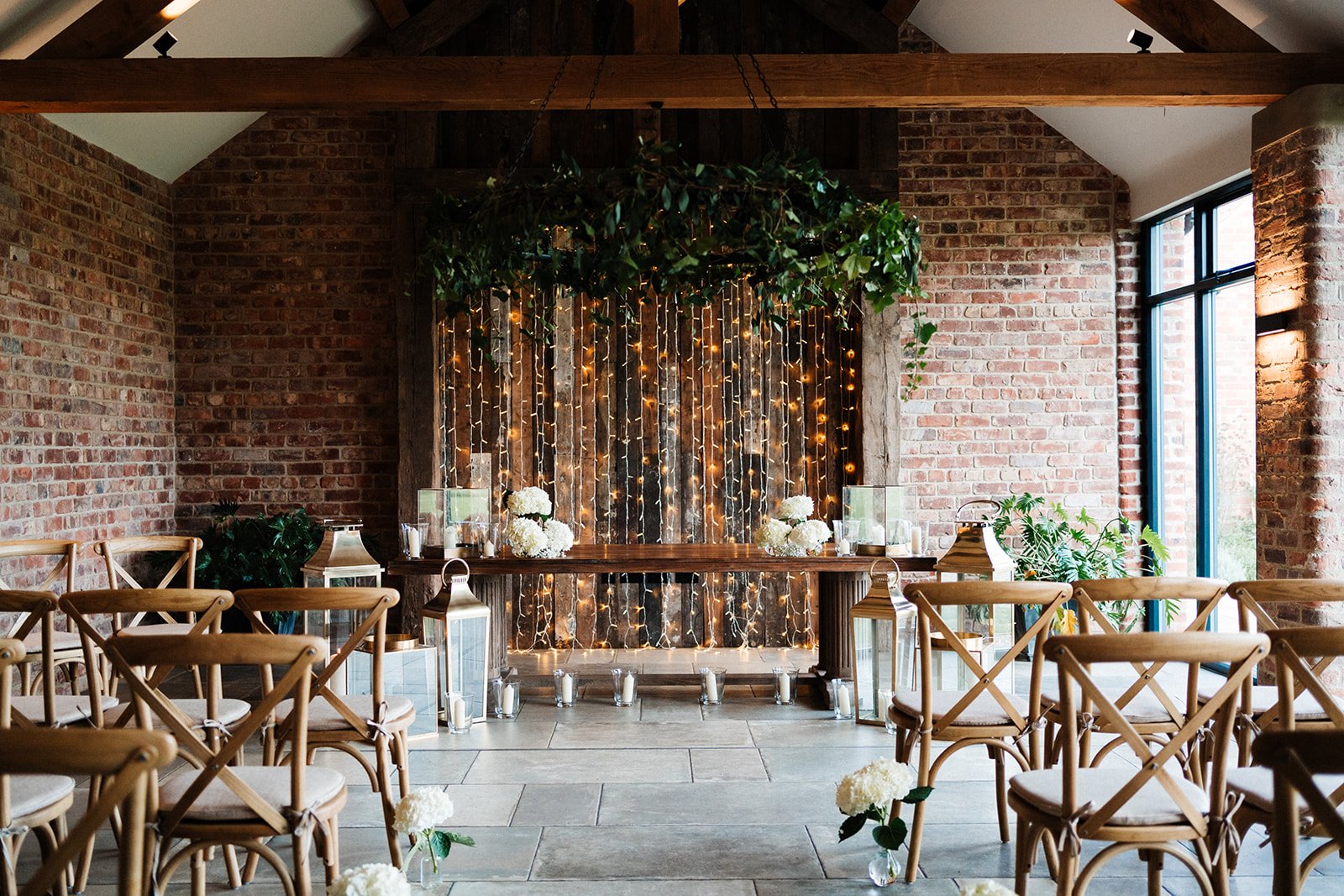 A barn room set up for a wedding ceremony at Thirsk Lodge Barns with wooden chairs and white details