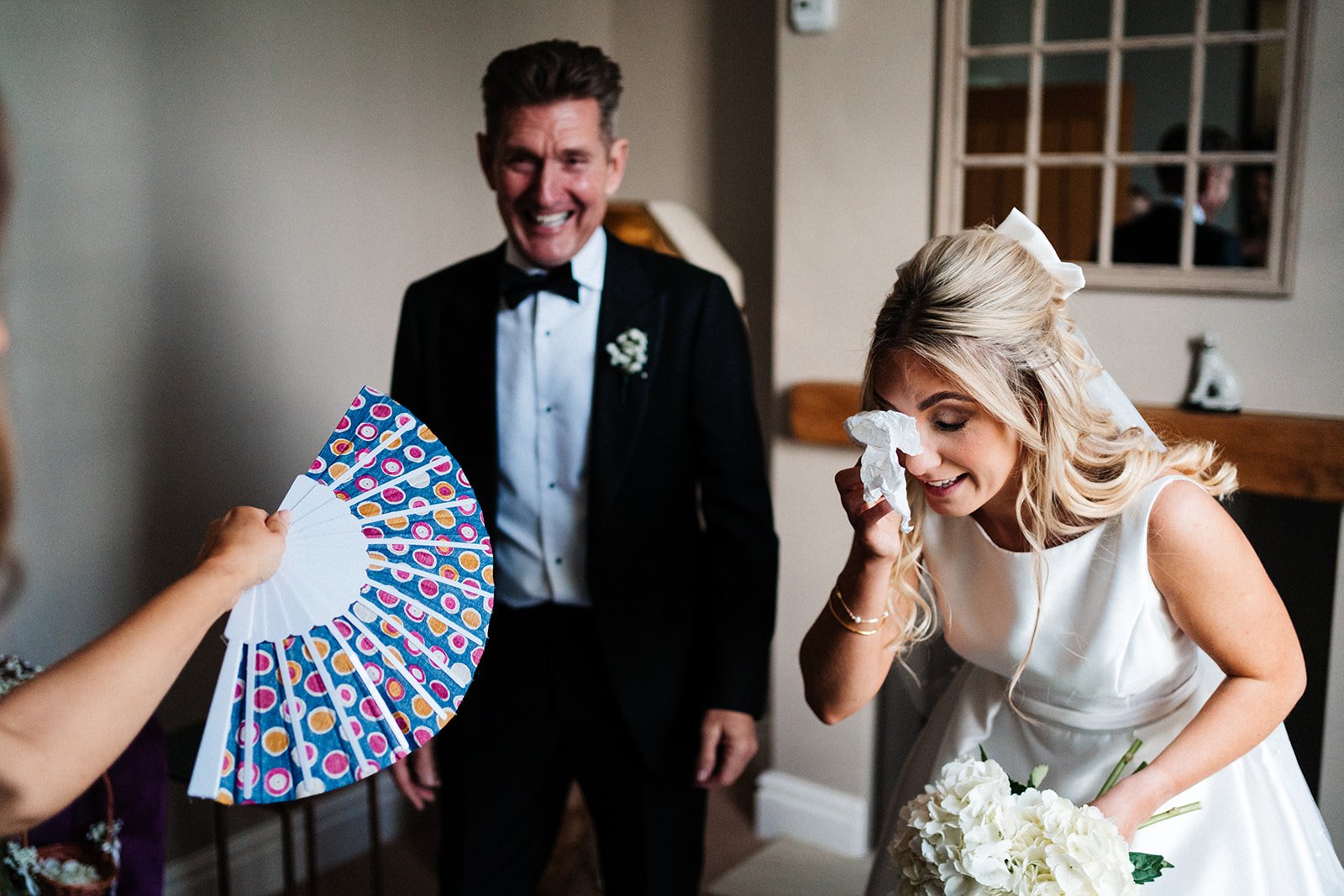 A bride holds a tissue to her eye as she stands next to her dad. Wedding at Thirsk Lodge Barns