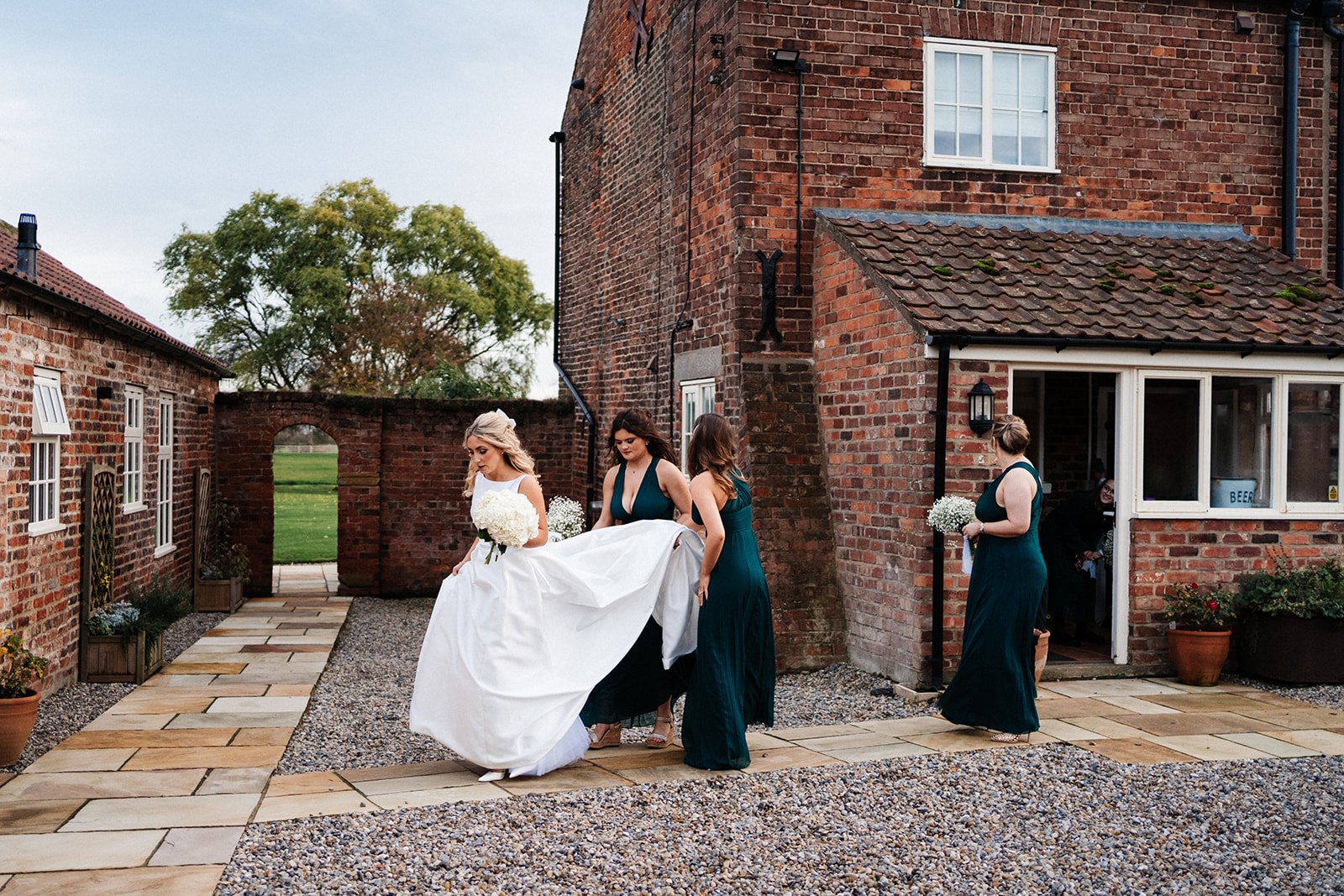 Bridesmaids help the bride with her dress walking from a country house