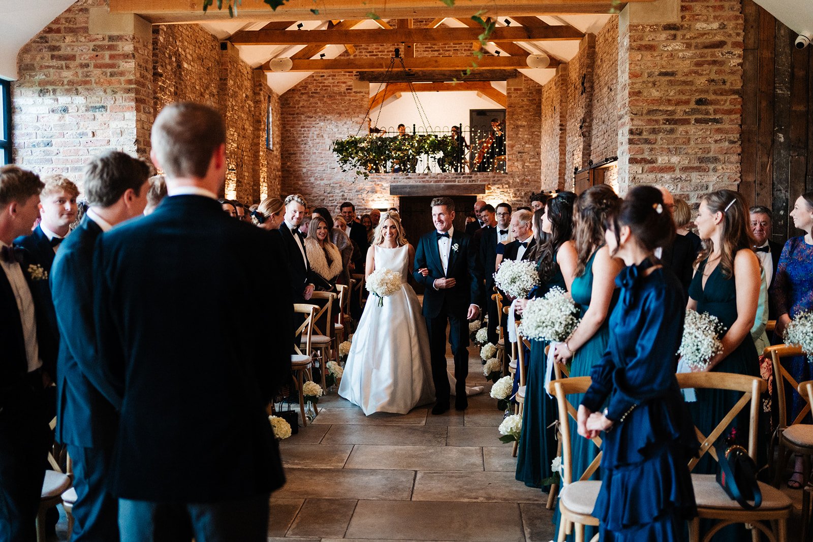 The bride and her father walk down the aisle in a barn ceremony room in North Yorkshire